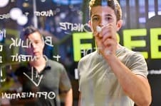 An image of a man in a T-shirt writing something on a glass wall from the other side.